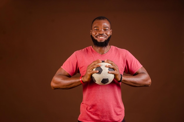 Photo of soccer team trendy african black funny captain wearing\
red tshirt holding soccer ball prepared to win local cup