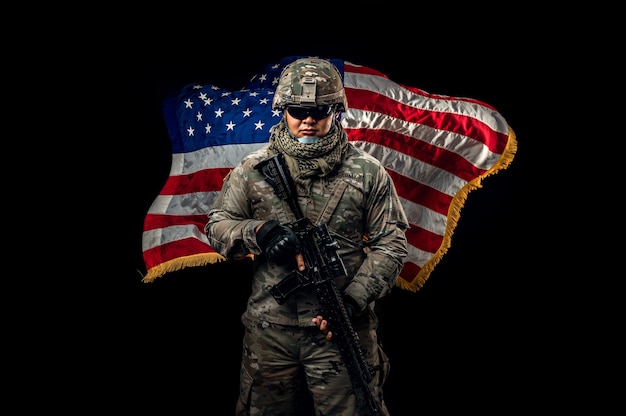 Photo of soldier holding the USA flag in background. Special force United States soldier or military contractors holding rifle. Image on background. soldier, army, war, weapon and technology concept.