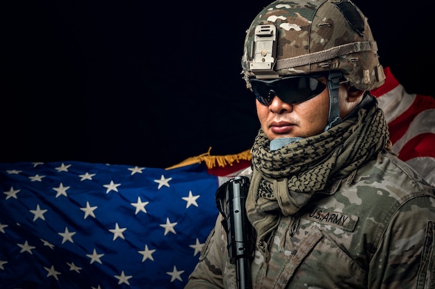 Photo photo of soldier holding the usa flag in background. special force united states soldier or military contractors holding rifle. image on background. soldier, army, war, weapon and technology concept.