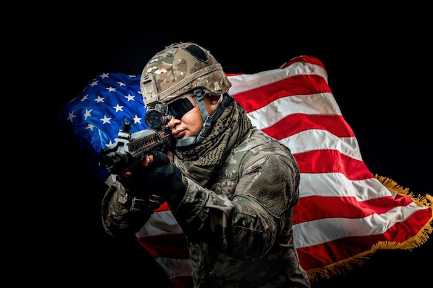 Photo of soldier holding the usa flag in background. special\
force united states soldier or military contractors holding rifle.\
image on background. soldier, army, war, weapon and technology\
concept.