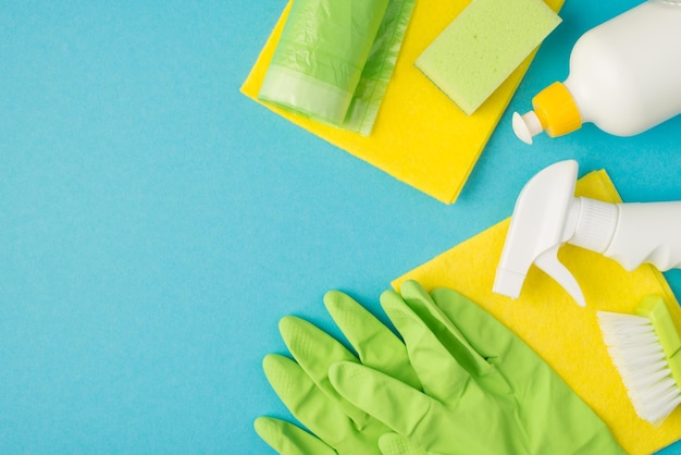 Above photo of sponge brush soap cleaning rag spray garbage bag and green gloves isolated on the blue background