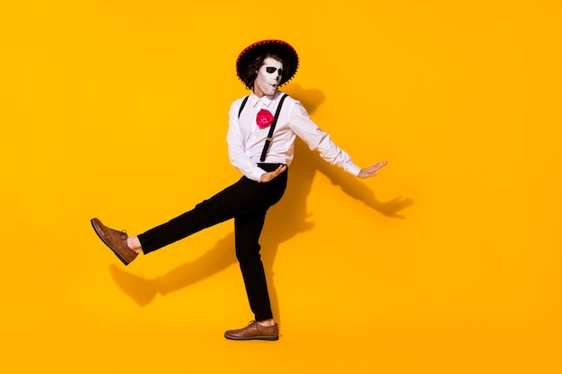 Photo of spooky ghost guy dance spanish latin dance carefree festival hands eyes closed wear white shirt death costume sugar skull suspenders pants shoes isolated yellow color background