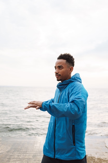 Photo of a strong handsome young african sports man outdoors at the beach sea walking make exercises.