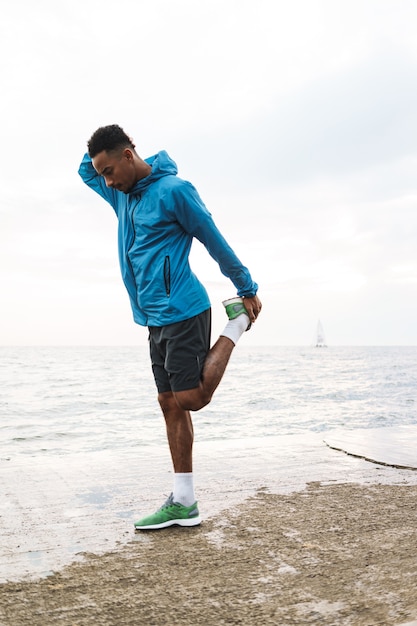 Photo of a strong handsome young african sports man outdoors at the beach sea walking make exercises.