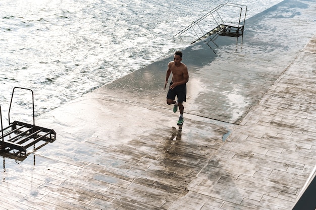 Photo of a strong handsome young african sports man runner outdoors at the beach sea running make exercises.