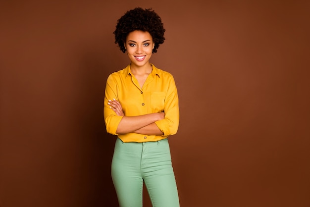 Photo of stunning business dark skin curly lady looking colleagues good mood arms crossed friendly smiling wear yellow shirt green pants isolated brown color