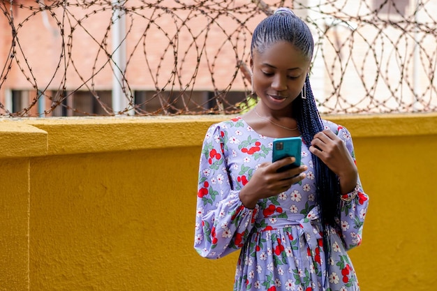 Photo of a stylish African woman in a vibrant dress captivated by her cell phone