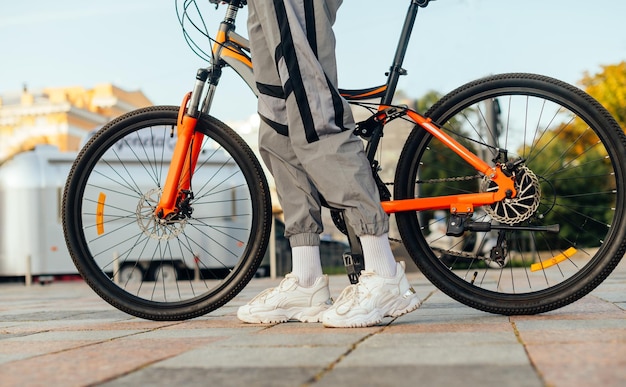 Photo of a stylish modern orange bicycle and female legs in\
fashionable sweat pants