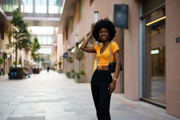 Foto di una giovane donna nera alla moda con i capelli ricci che indossa un top corto arancione che cammina per strada