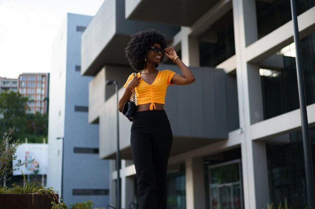 photo of a stylish young black woman with curly hair wearing orange crop top walking in the street