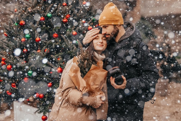 Photo of a stylish young couple in love posing for a photo during a light snowfall at the Christmas street fair