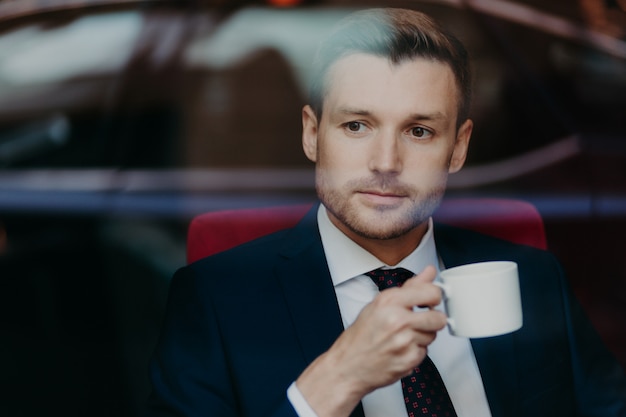 Photo of successful prosperous male entrepreneur with stubble,  wears formal clothes