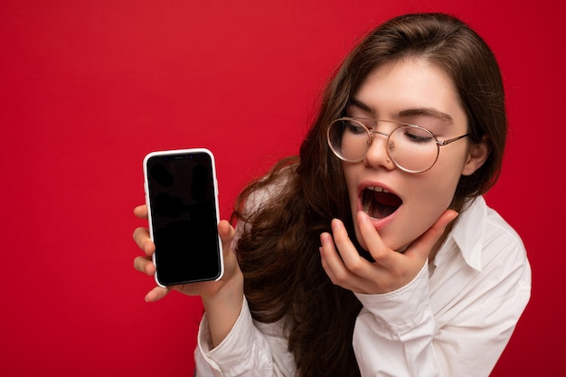 photo of surprised beautiful young brunette woman wearing white shirt and optical glasses isolated