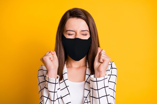 Photo of surprised businesswoman wearing black fabric face mask fists closed eyes isolated yellow color background