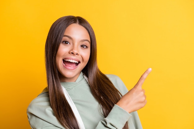 Photo of sweet charming child girl dressed casual green outfit pointing finger empty space isolated yellow color background