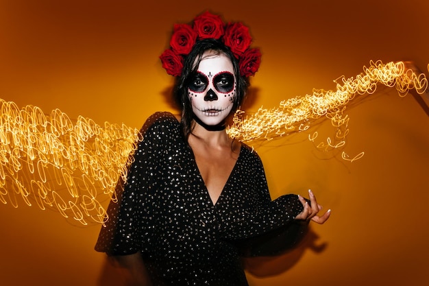 Photo taken in studio with fiery luminous background Lady with makeup in form of Mexican traditional skull image spends time at party