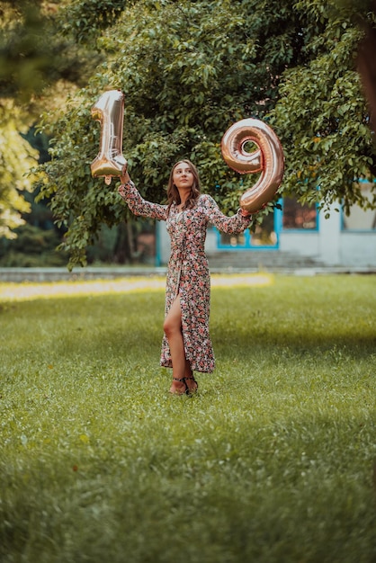 A photo of a teenage girl being photographed next to a birthday number in the park