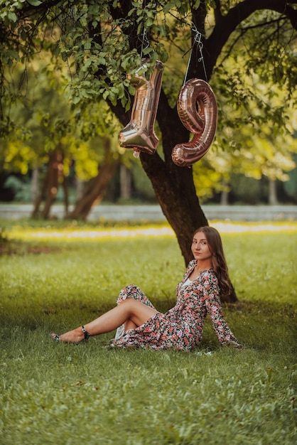 Фотография девочки-подростка, которую фотографируют рядом с номером дня рождения в парке.