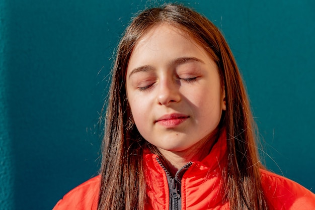 Photo of teenage girl on a turquoise wall. Teenager girl in orange jacket. portrait,