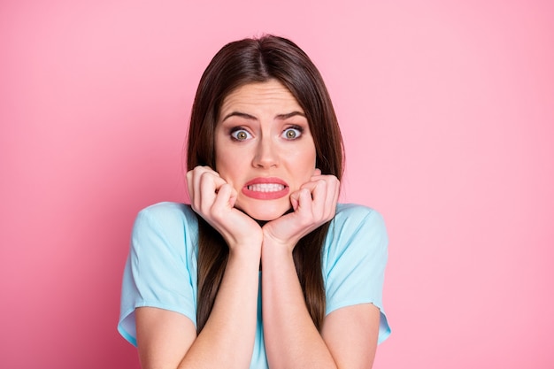 Foto di una donna terrorizzata con le braccia sul mento e gli occhi pieni di paura indossano una maglietta blu casual isolata con uno sfondo di colore rosa pastello