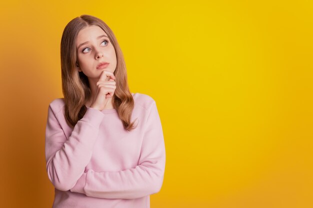 Photo of thoughtful girl finger chin look empty space on yellow background