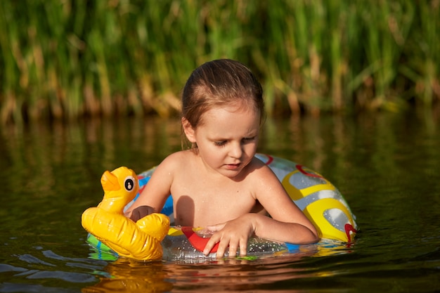 Photo of thoughtful little fair haired girl having pensive look at water surface