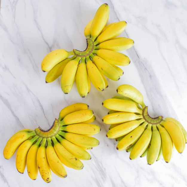 Photo photo of three indonesia yellow bananas on the white marble background