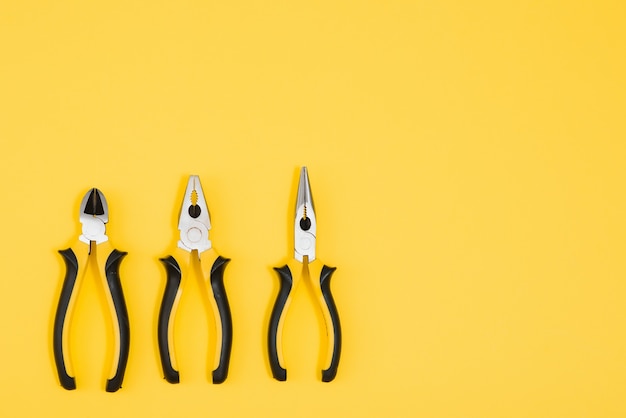 Photo of three yellow and black pliers isolated on yellow background