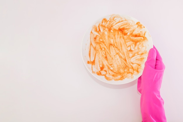 Photo top view of hands in pink rubber gloves holding white dirty plate on isolated white background with copy space.