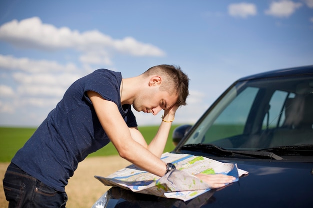 旅行者が道路脇に車を停め、道に迷って地図を読んでいる写真。地図と男性に焦点を当てます。