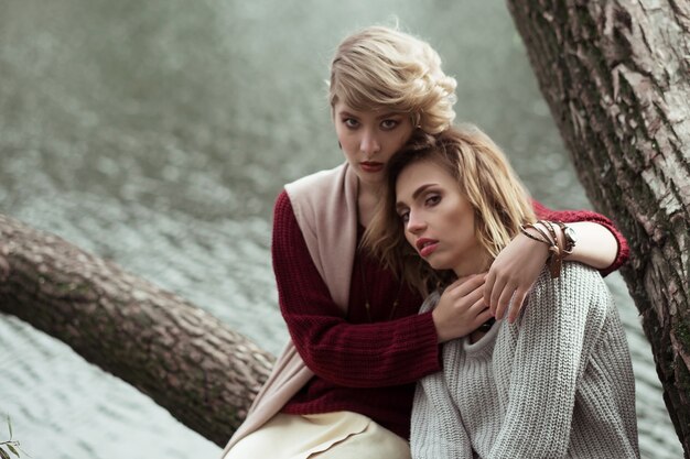 Photo of a two beautiful women posing on a tree near lake.