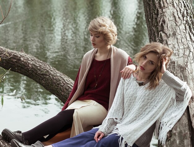 Photo of a two beautiful women posing on a tree near lake.