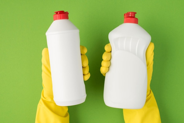 Above photo of two bottles of detergent in hands isolated on the green background