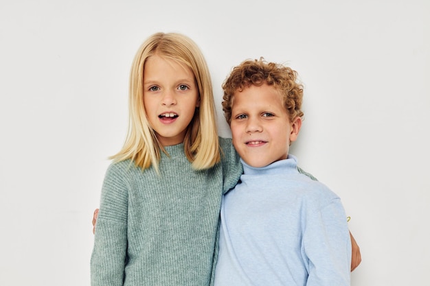 Photo of two children in multicolored sweaters posing for fun light background