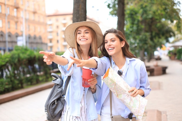 Photo of two girls enjoying sightseeing outdoor. Beautiful female tourists exploring city with map.