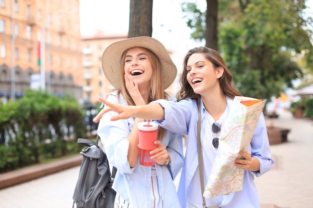 Photo of two girls enjoying sightseeing outdoor. Beautiful female tourists exploring city with map.