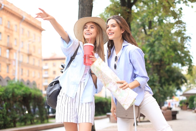 Photo of two girls enjoying sightseeing outdoor. Beautiful female tourists exploring city with map.