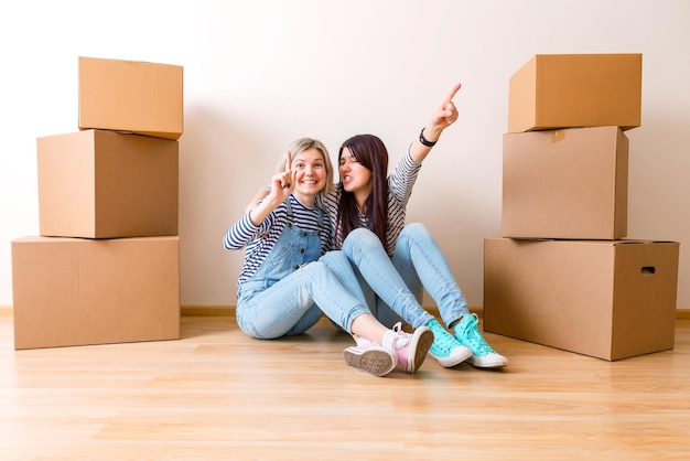 Photo of two girls sitting on floor among cardboard boxes