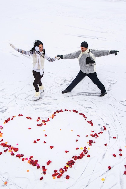 Photo of two lovers man and woman skating near the heart of rose petals on the snow