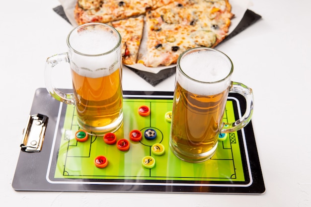 Photo of two mugs of beer, table football, pizza on white table