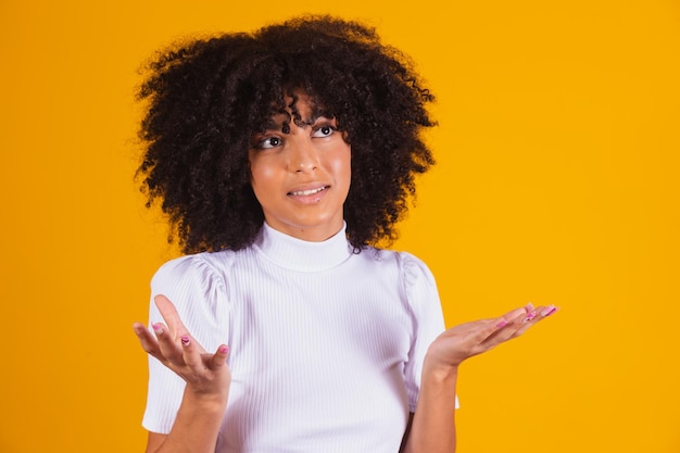 Photo of unconscious woman raises palms hesitantly, faces difficult choice, has questioning expression, says don't know, wears casual shirt, isolated on yellow background. I do not care