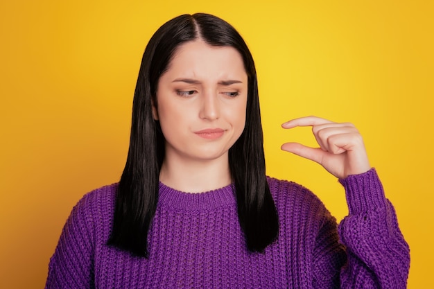 Photo of unimpressed dissatisfied woman measures fingers sign demonstrates something little isolated over yellov color background