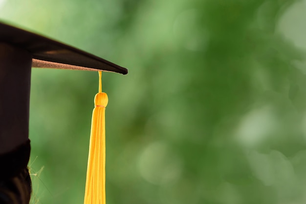 Behind photo of university graduate wears gown and black cap, yellow ribbon