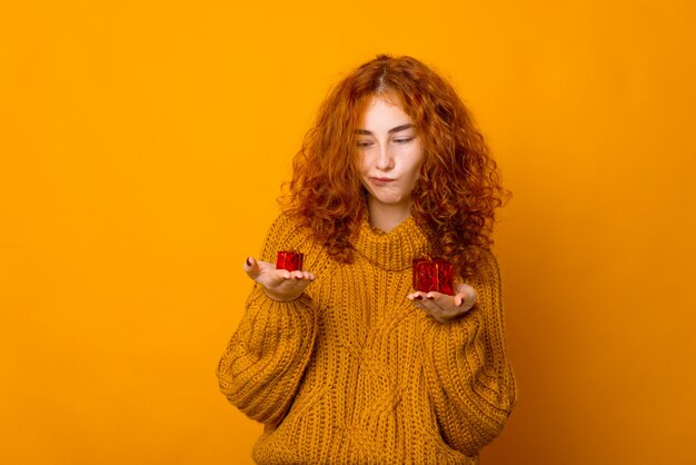 Photo of unsatisfied ginger girl, looking confused at small gift boxes, over orange background