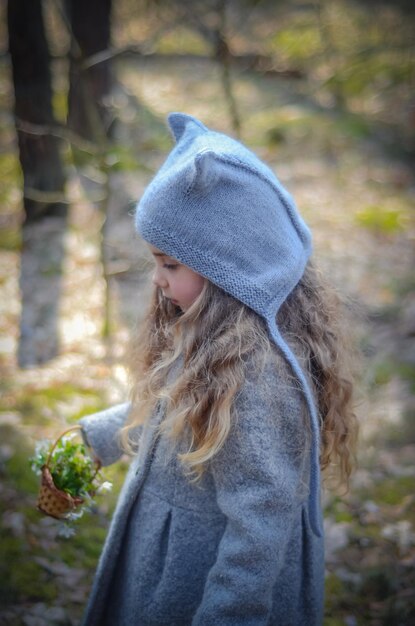 Photo of vintage dressed girl playing with flower basket in the forest.