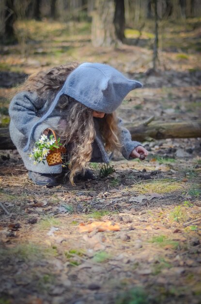 Фотография винтажно одетой девушки, играющей с цветочной корзиной в лесу.