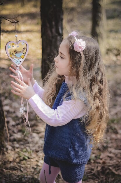 Photo of vintage dressed girl playing with wooden decoration in the forest.