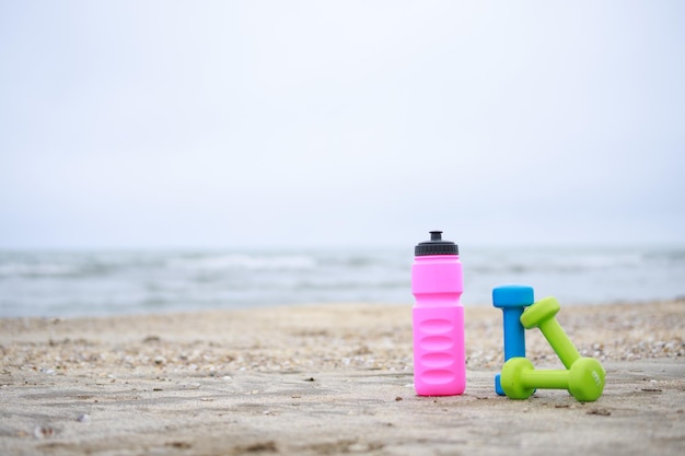 Photo of water bottle and dumbbells at the beach High quality photo