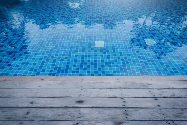 Foto di acqua in una piscina con riflessi di sole e passerella in legno.