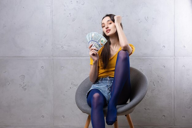 Photo of a wealthy woman in simple clothes holding a fan of dollar money isolated against a concrete wall background